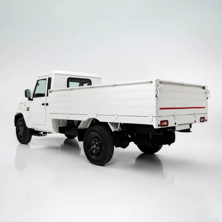 Rear three-quarters view of a white flatbed utility truck on a reflective studio floor, showing the cargo bed and dual rear tires.