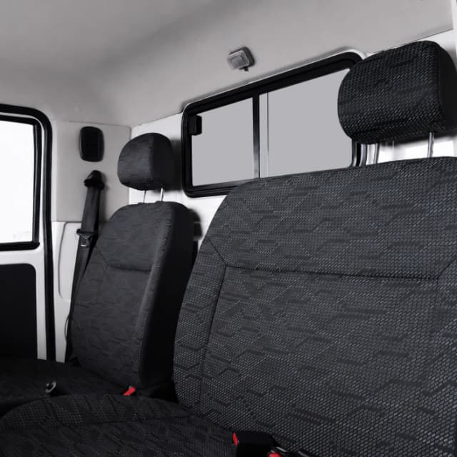 Interior of a vehicle showing front and back seats with dark patterned upholstery and headrests, window and seat belts visible on the left side.