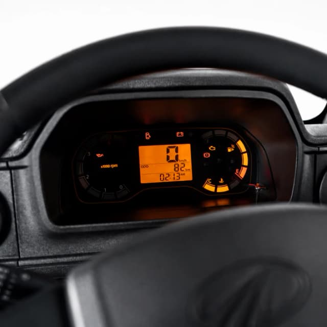 View from the driver's seat of a car dashboard; digital display shows speed 0, with orange backlit gauges.